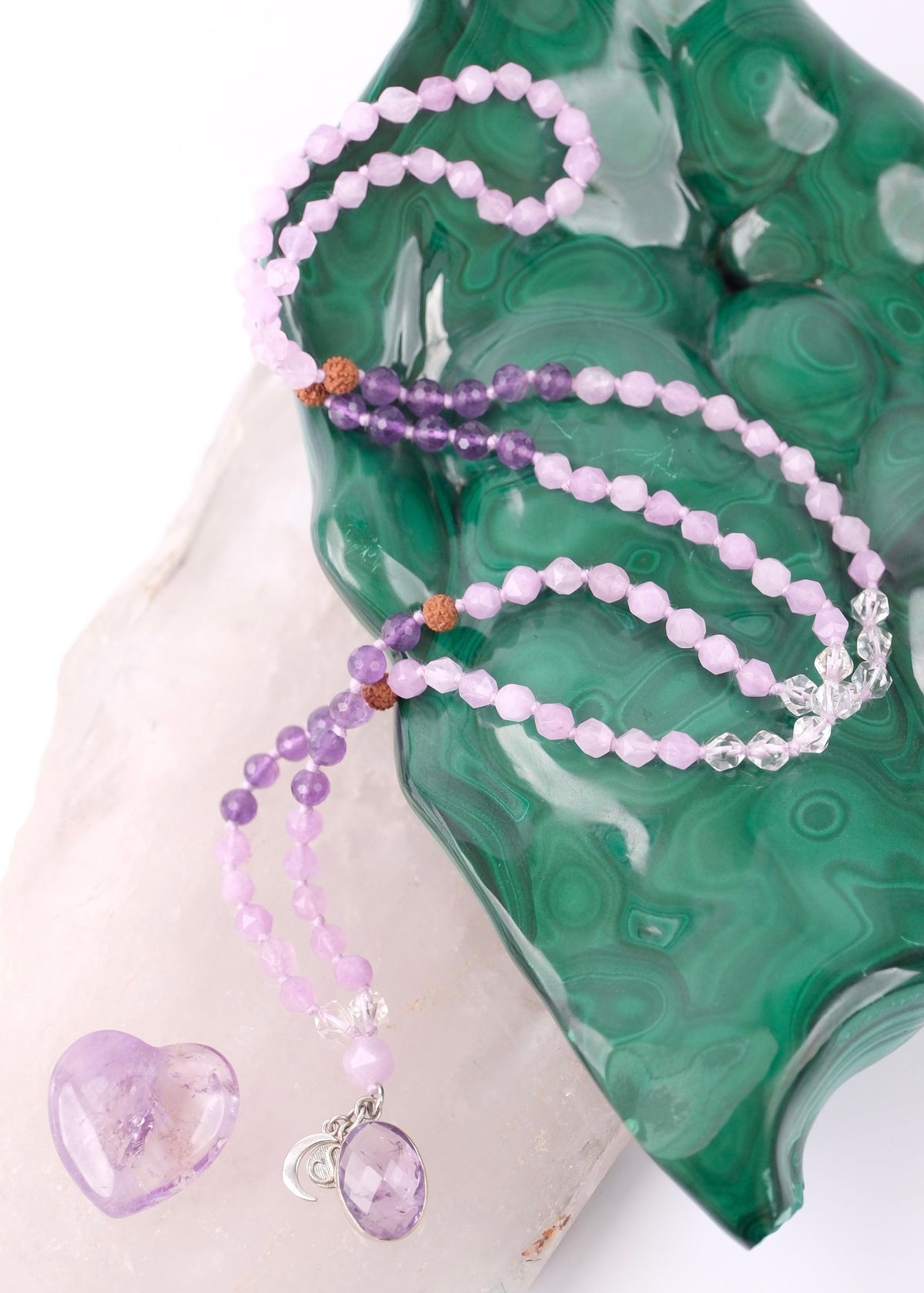 Purple beaded necklace with a heart charm on a green stone surface