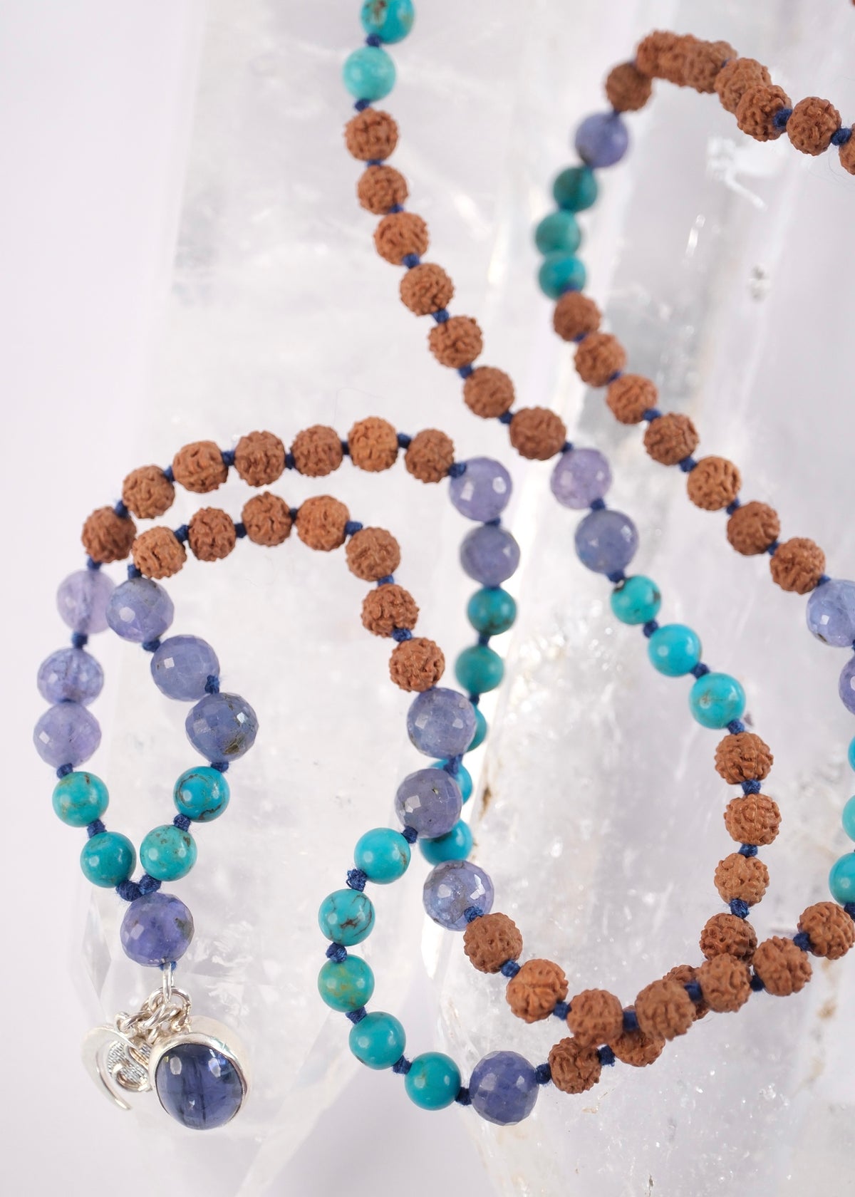 Divya Chakshu mala of the awakened seer with faceted tanzanite, old Persian turquoise, Rudraksha, and a premium iolite pendant in sterling silver. Handcrafted. Resting on Crystal background