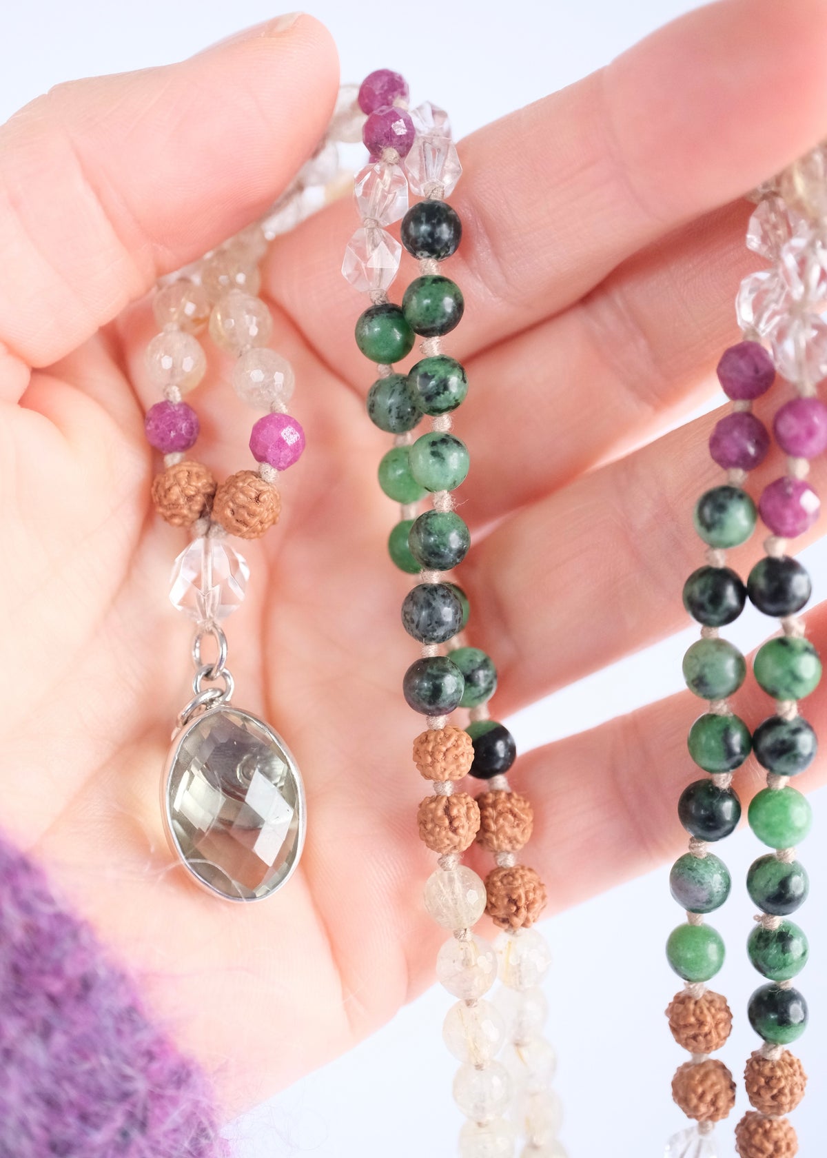 hand holding beaded mala necklace of zoisite, ruby and lemon quartz pendant