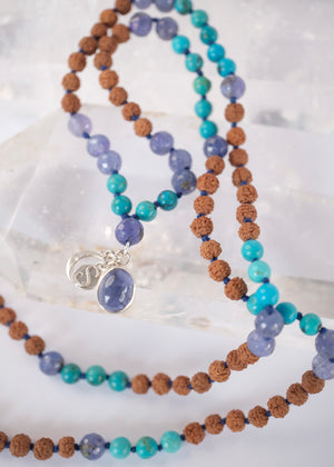 Tanzanite, Persian turquoise, and Rudraksha japa mala resting on selenite, finished with crescent moon and S charms.