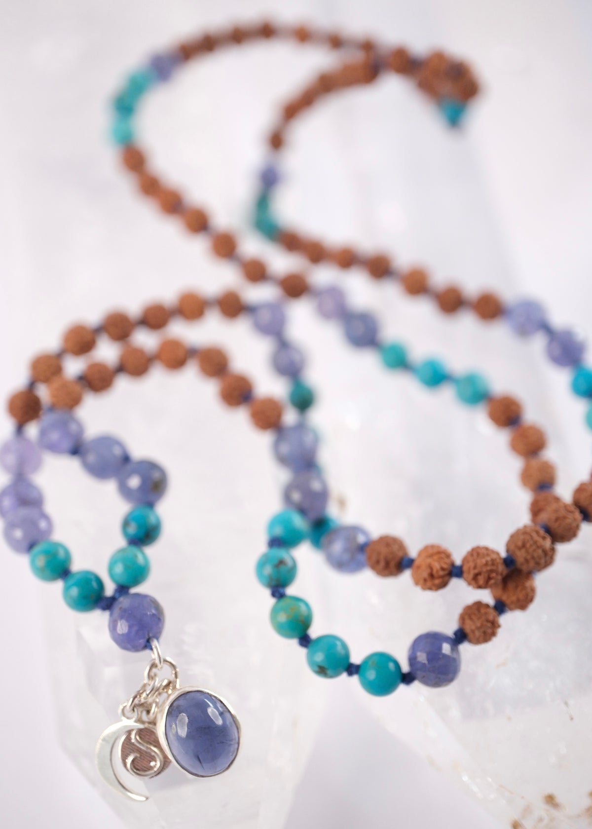 Tanzanite, Persian turquoise, and Rudraksha japa mala resting on selenite, finished with crescent moon and S charms.