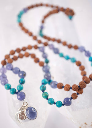 Tanzanite, Persian turquoise, and Rudraksha japa mala resting on selenite, finished with crescent moon and S charms.