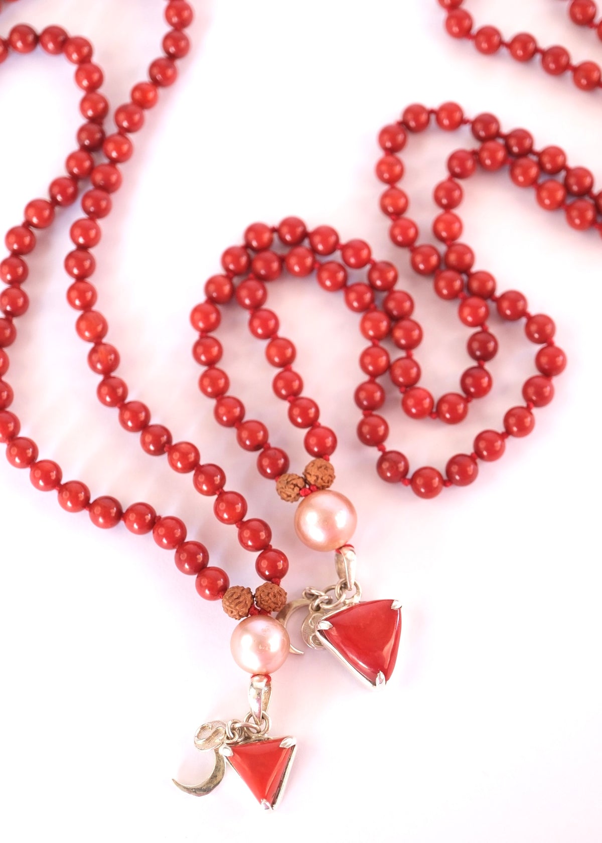 A red beaded necklace with pink pearl-like beads, brown textured spacers, and two dangling red triangular charms with silver-toned metal details, photographed on a white background.