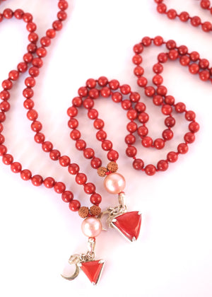 A red beaded necklace with pink pearl-like beads, brown textured spacers, and two dangling red triangular charms with silver-toned metal details, photographed on a white background.