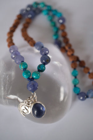 Tanzanite, Persian turquoise, and Rudraksha japa mala resting on selenite, finished with crescent moon and S charms.