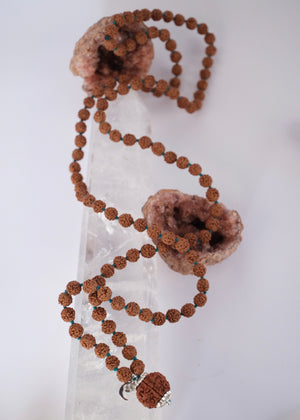Shivoham Premium collector's Rudraksha japa mala for courage, wisdom, focus, and clarity, finished with sterling silver caps and charms. Authentic Nepal Rudraksha mala resting on clear quartz crystal
