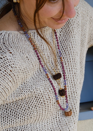 A hand holding a beaded necklace featuring a large pink ruby, faceted purple amethyst beads, rudraksha, ruby and tanzanite