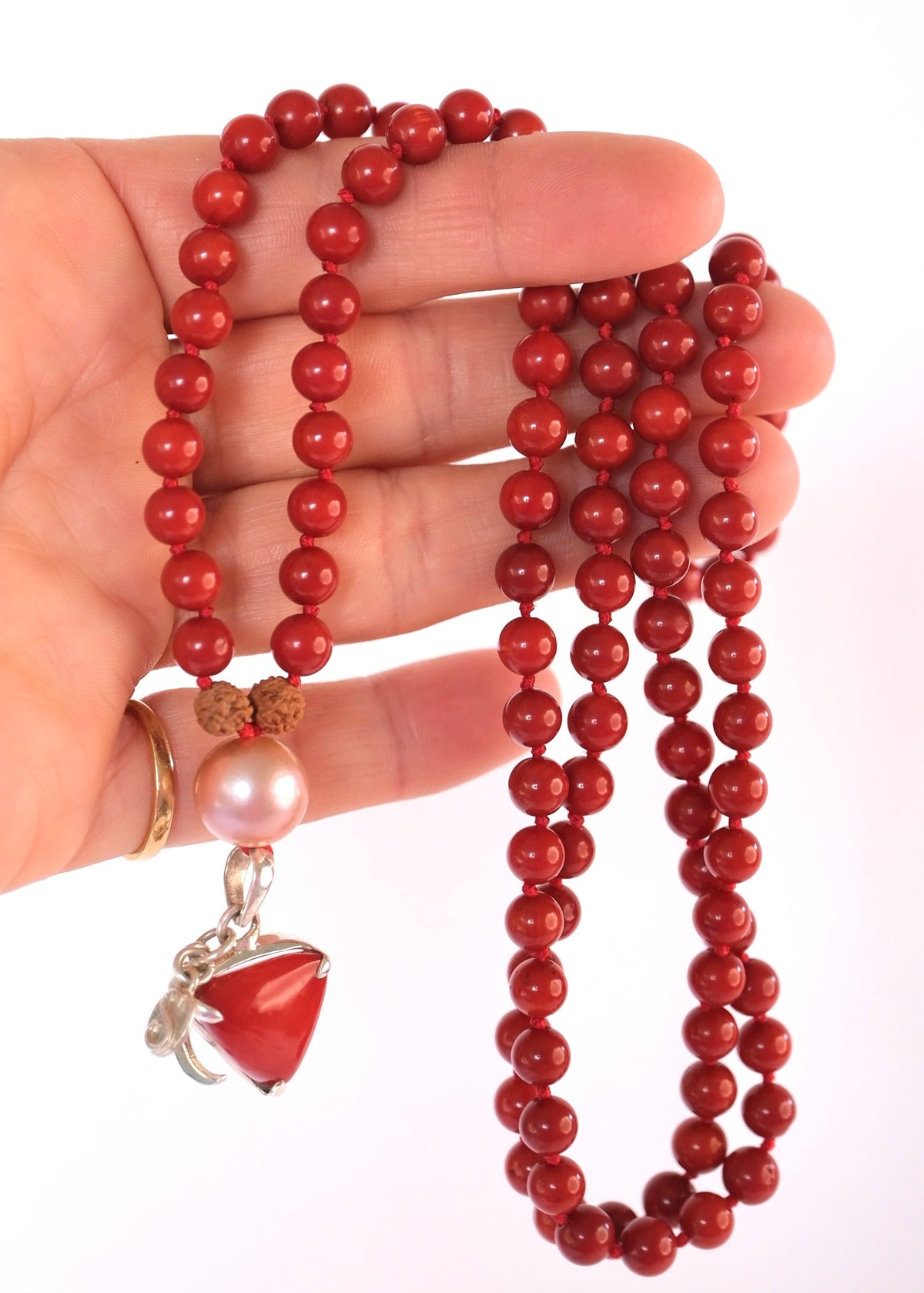 Hand holding coral mala bead necklace with large coral pendant