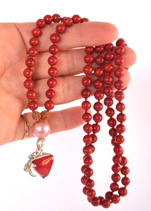A red beaded necklace with pink pearl-like beads, brown textured spacers, and two dangling red triangular charms with silver-toned metal details, photographed on a white background.
