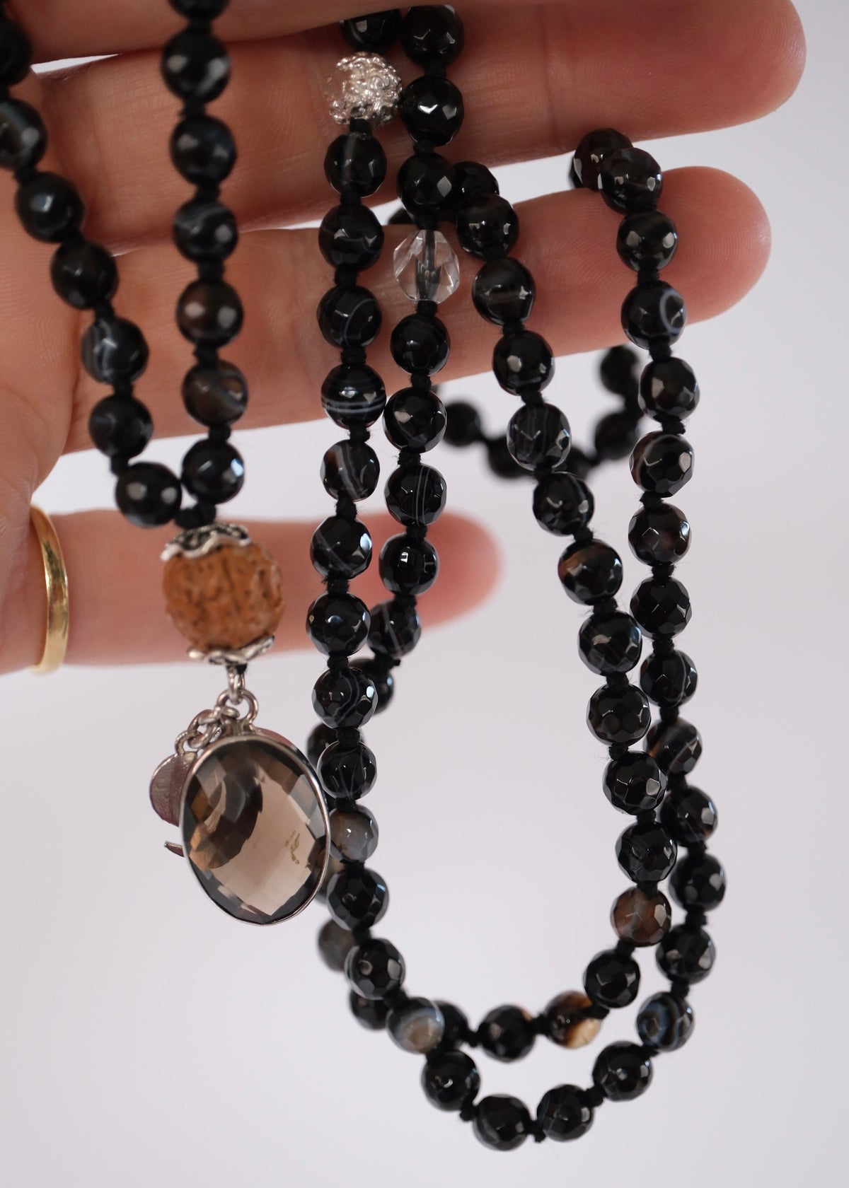 Close view of the faceted smoky quartz pendant with crescent moon and S charms on the Vajra mala.