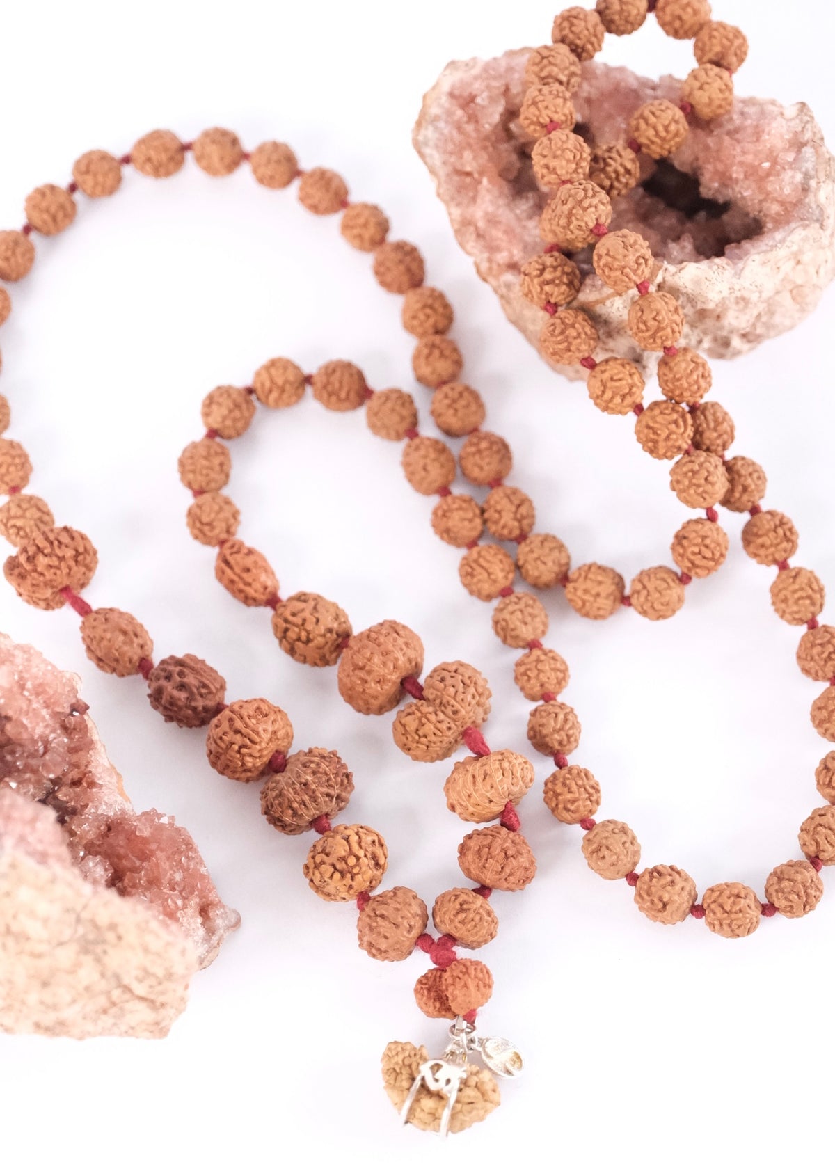 Handcrafted pure Rudraksha Siddha Mala resting on rose quartz, carrying every mukhi from one to fourteen.