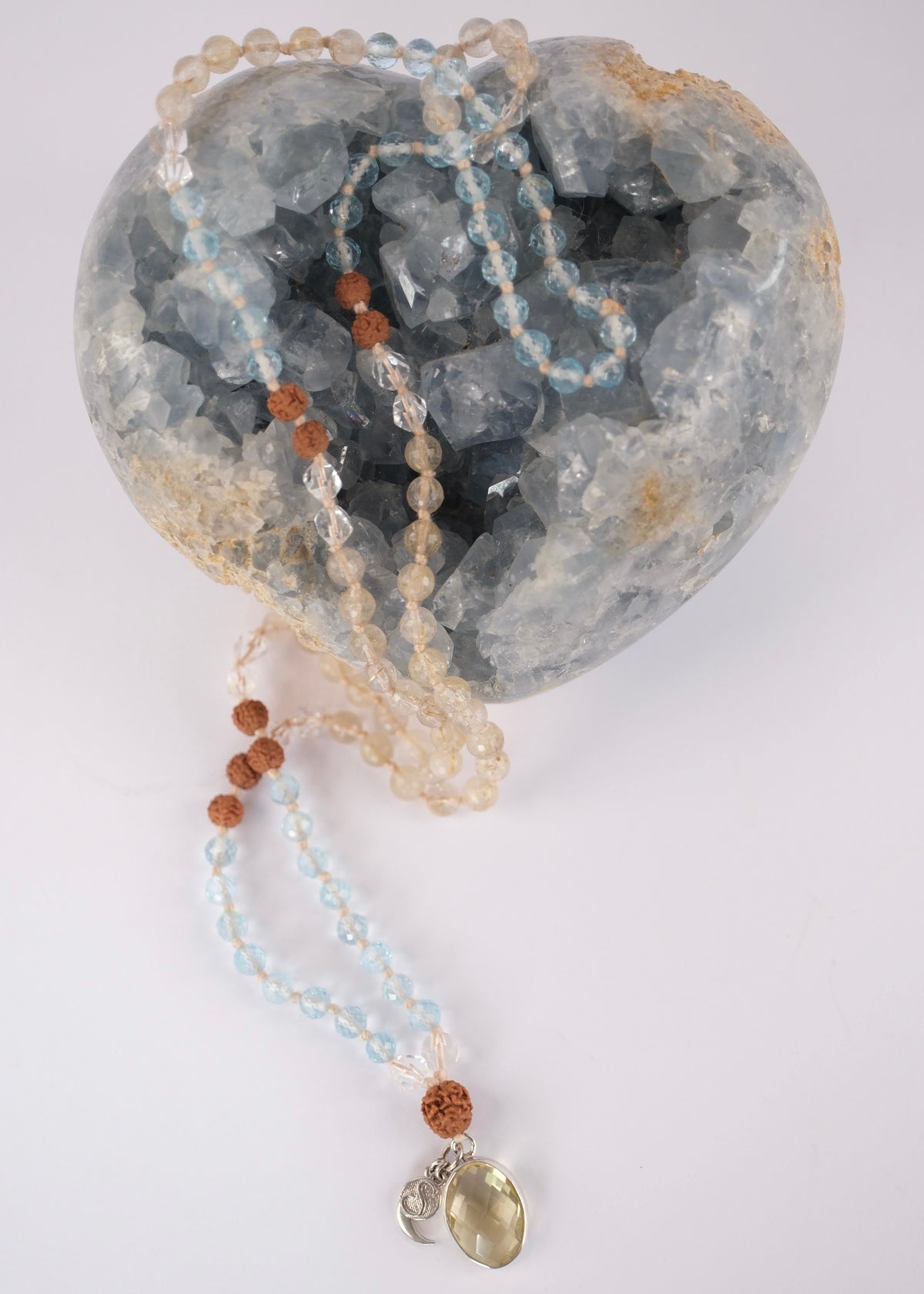 Soft blue topaz and clear quartz prayer mala for peace, calm, and mental clarity, threaded with warm golden rutilated quartz. Sitting on a blue crystal heart