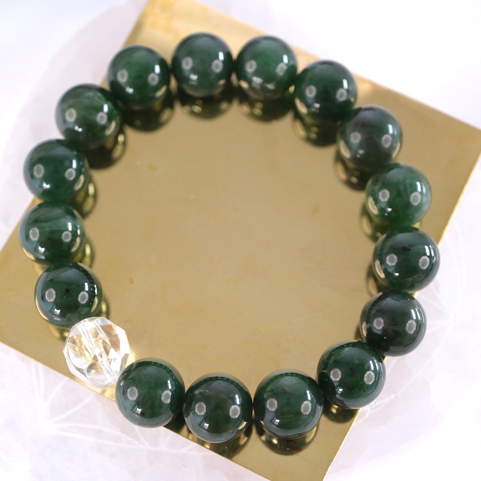 Deep green jade bracelet resting on gold, the treasured Stone of Heaven for abundance and peace.