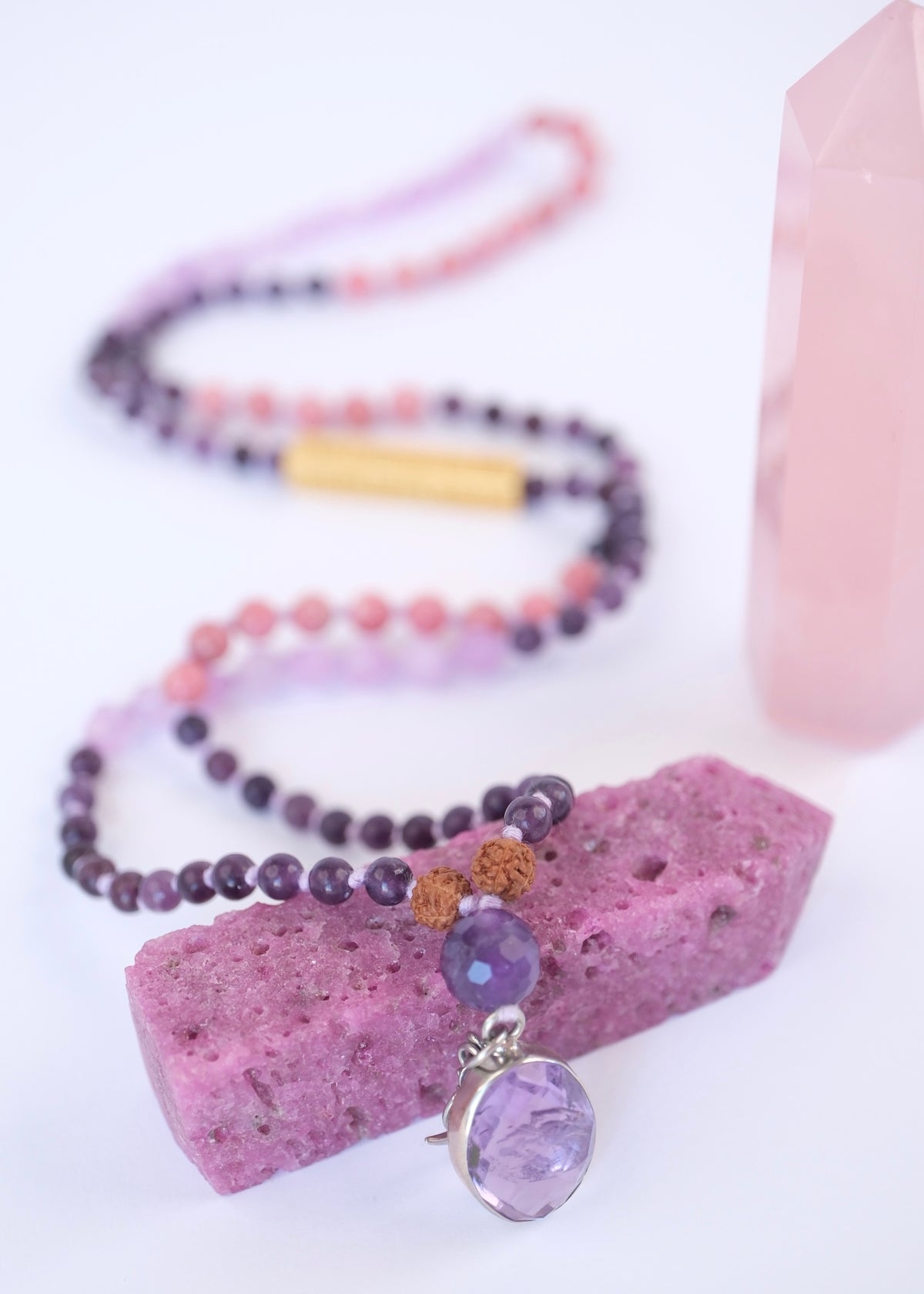 Purple beaded necklace with amethyst pendant on a white background