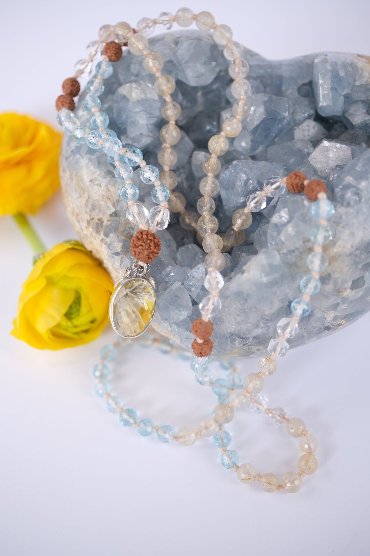 Pale blue and golden topaz japa mala resting on a celestite heart, finished with sterling silver and lemon quartz.