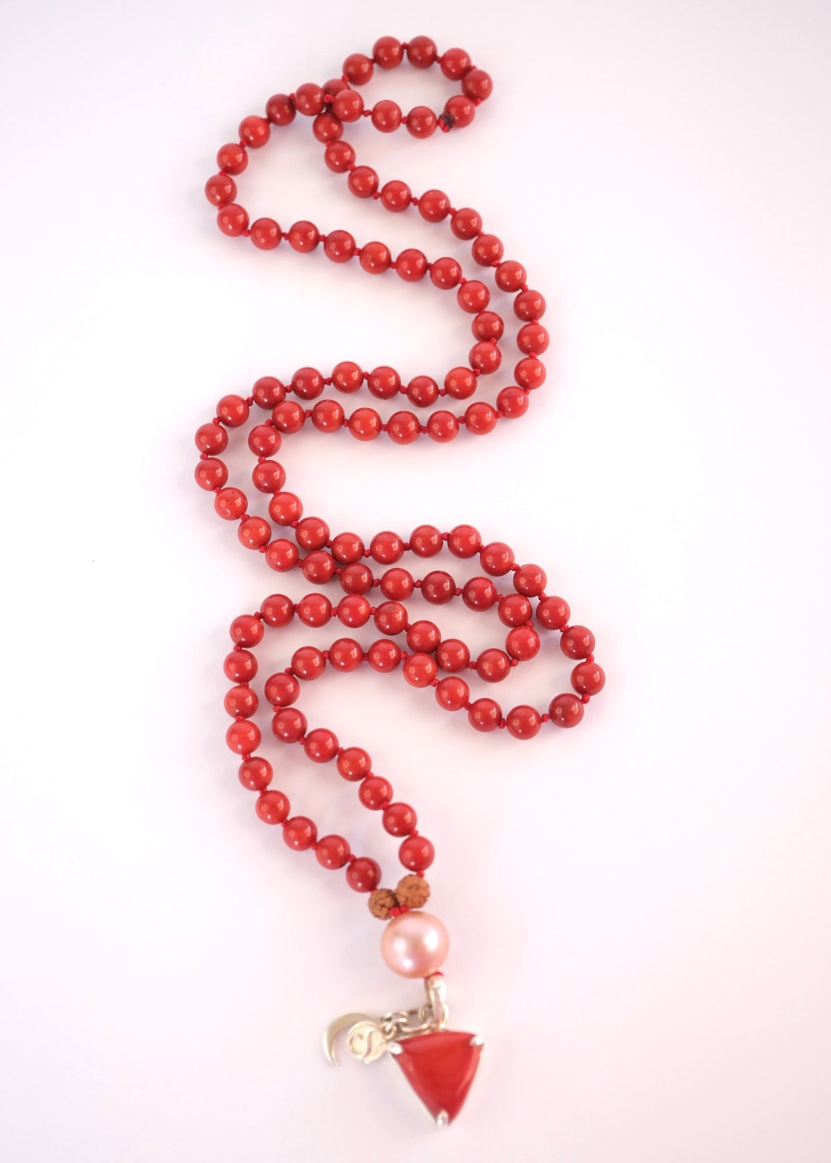 Triangular Italian red coral Moonga pendant carved in the sacred downward triangle of Mars
Detail of premium Italian red coral pendant on the Moonga Mars mala
Rare twelve millimetre pink Akoya pearl guru bead glowing above red coral beads
Strand of natural Taiwanese red coral beads with two Rudraksha on the Moonga Mala
Sterling silver Shivoham crescent moon and S charms on the red coral Mars mala