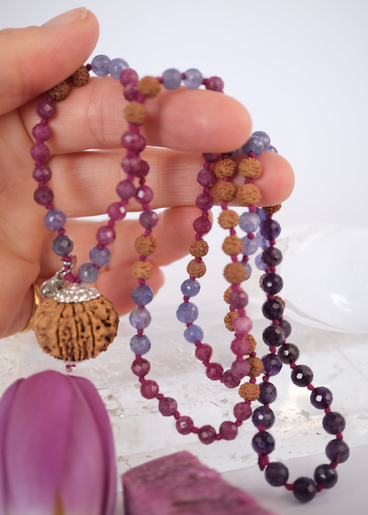 Hand holding Durga warrior priestess mala with faceted ruby, tanzanite, amethyst and nine mukhi Rudraksha