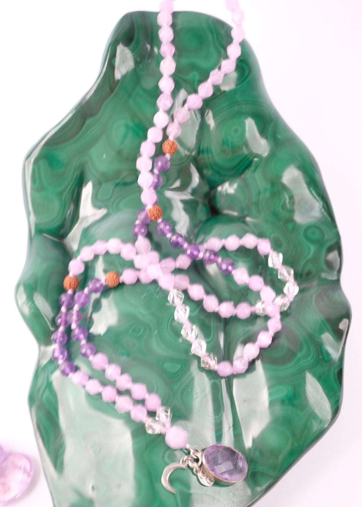 Beaded necklace with purple and pink stones on a green stone surface