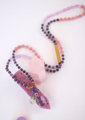 Purple beaded necklace with amethyst pendant on a white background
