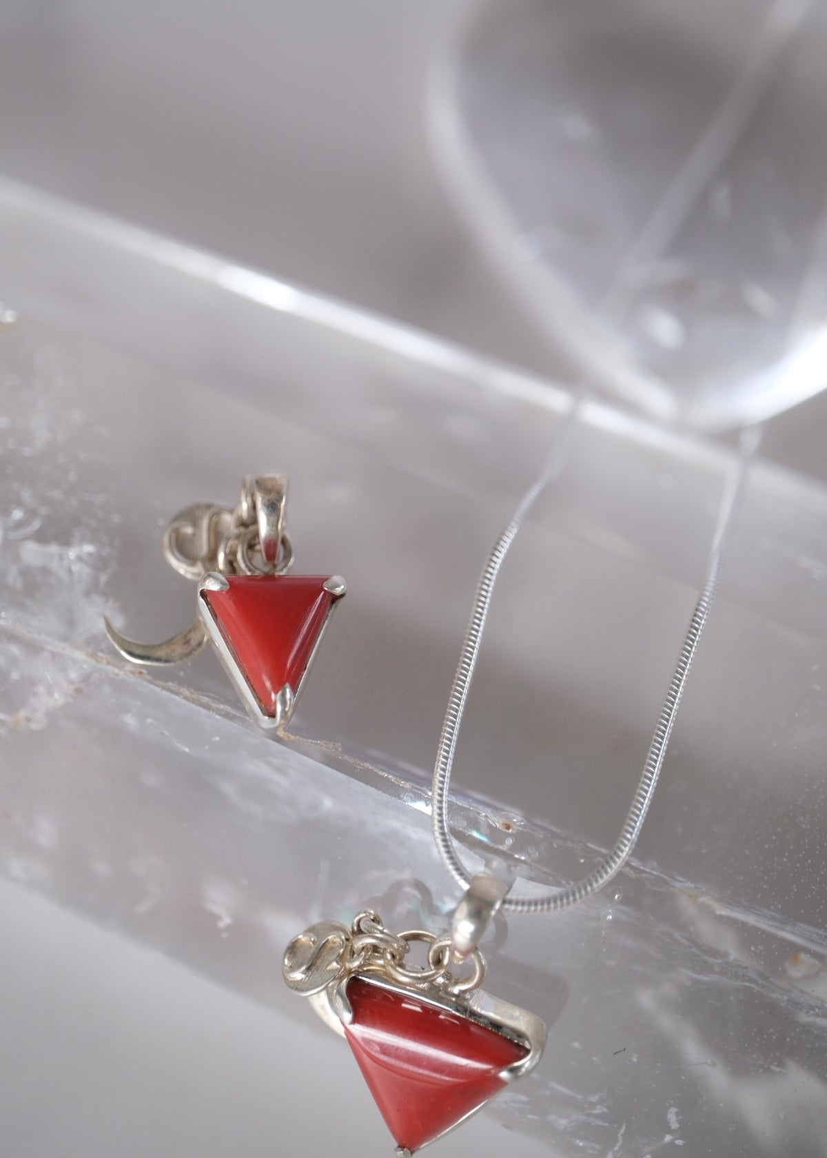 Two sizes of Italian red coral Mars yantra pendant in sterling silver, small and large, with chain resting over clear quartz.