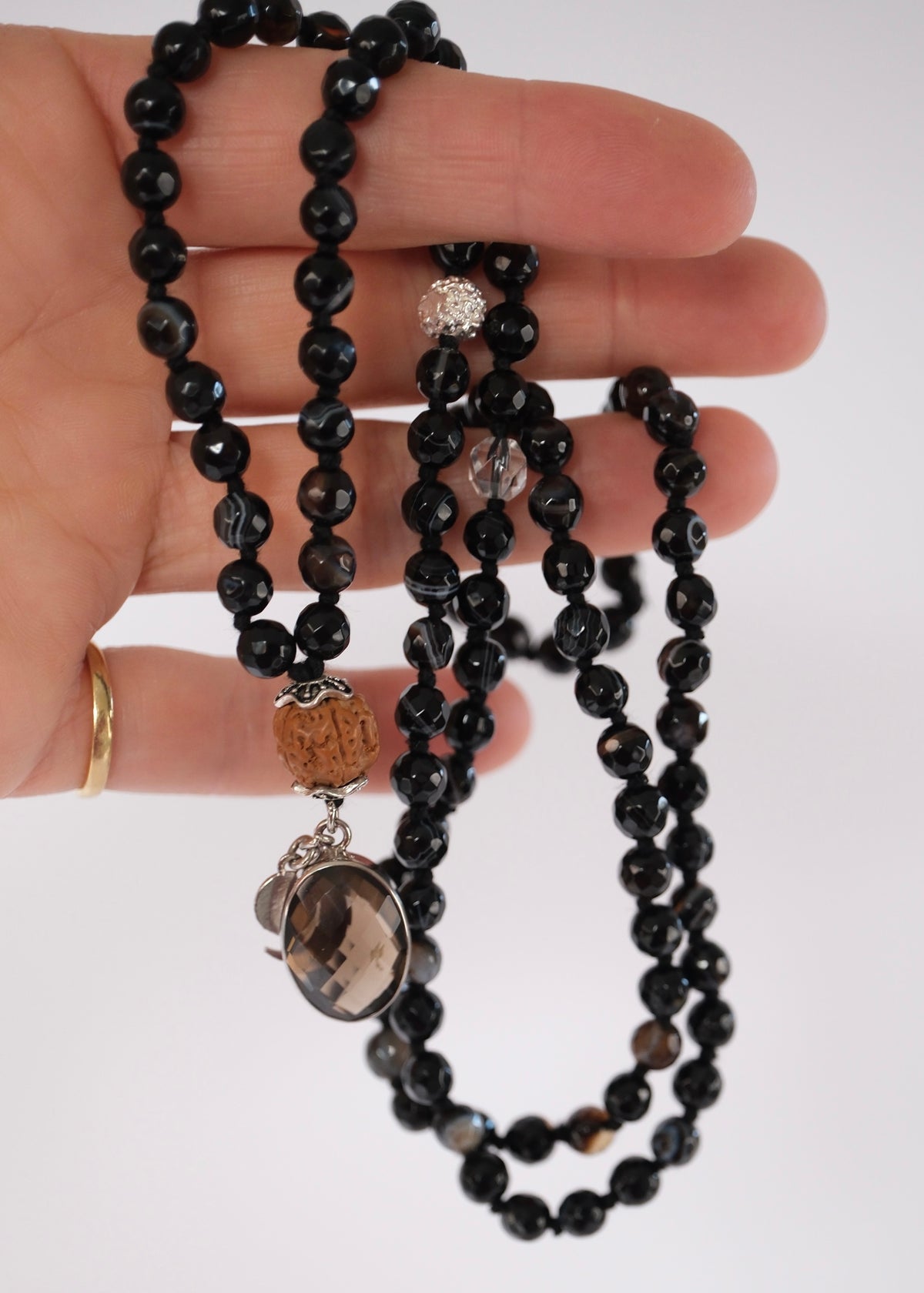 Hand holding up a Close view of the faceted smoky quartz pendant with crescent moon and S charms on the Vajra mala.