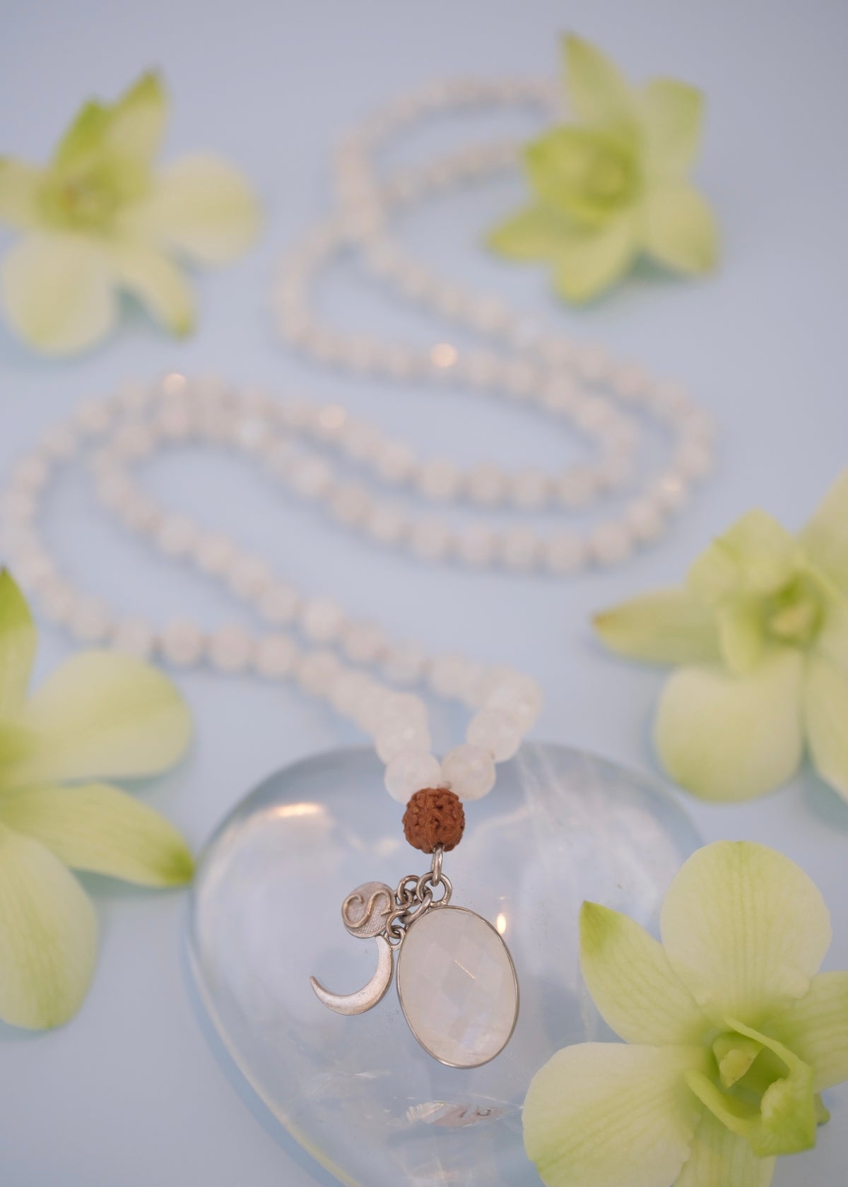 Moonstone Mala Necklace with charms on a clear heart-shaped object surrounded by green flowers