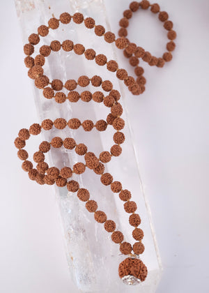 Shivoham Premium collector's Rudraksha japa mala for courage, wisdom, focus, and clarity, finished with sterling silver caps and charms. Authentic Nepal Rudraksha mala resting on clear quartz crystal