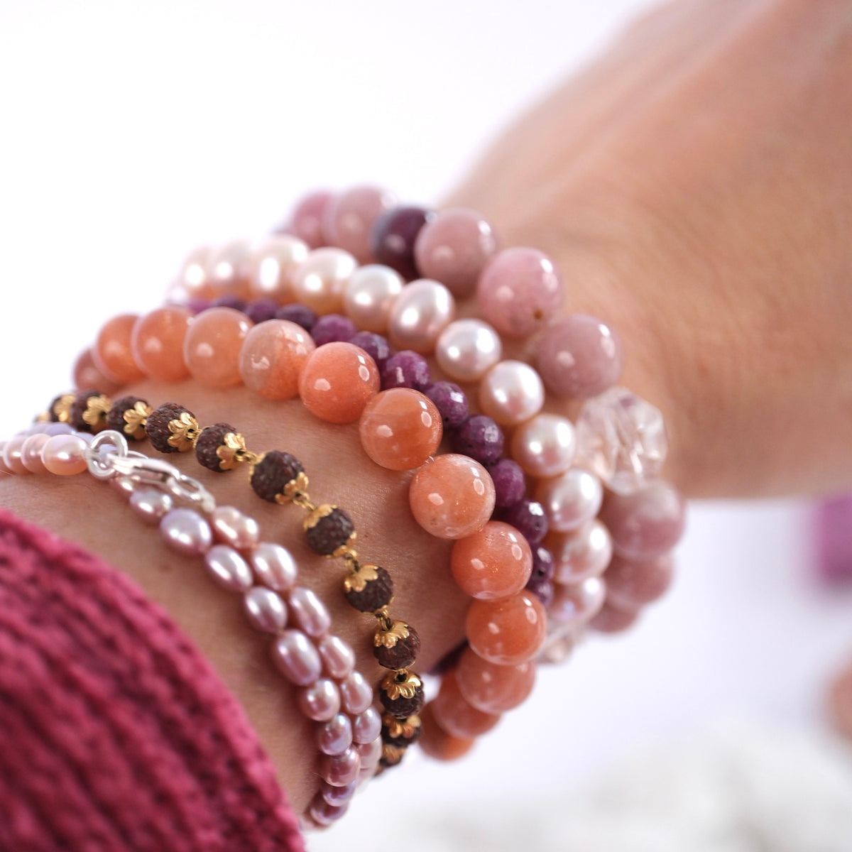 BRACELET STACK WITH SEVERAL PINK TONES OF CRYSTALS and small rudraksha with gold caps. Worn on woman's wrist