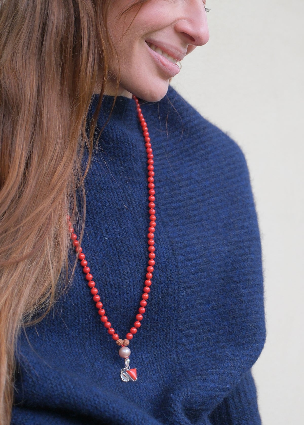 Woman in a blue jumper wearing the striking red coral Moonga Mars mala