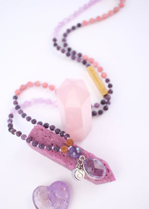 Purple beaded necklace with amethyst pendant on a white background