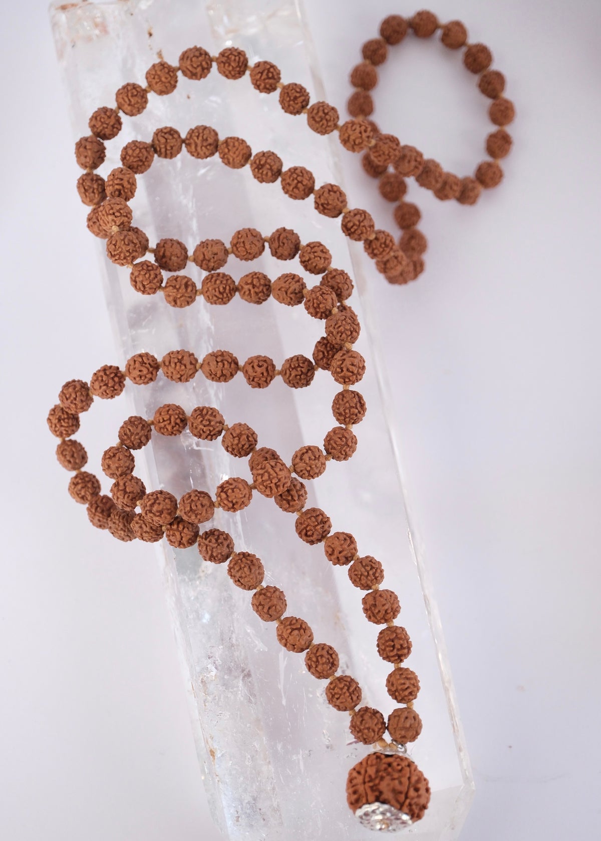 Shivoham Premium collector's Rudraksha japa mala for courage, wisdom, focus, and clarity, finished with sterling silver caps and charms. Authentic Nepal Rudraksha mala resting on clear quartz crystal
