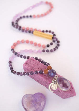 Purple beaded necklace with amethyst pendant on a white background