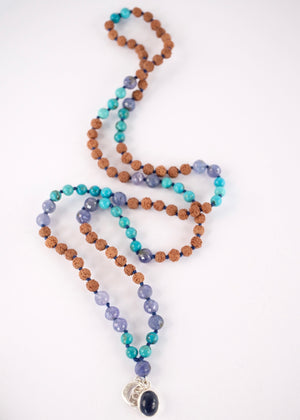 Tanzanite, Persian turquoise, and Rudraksha japa mala resting on selenite, finished with crescent moon and S charms.