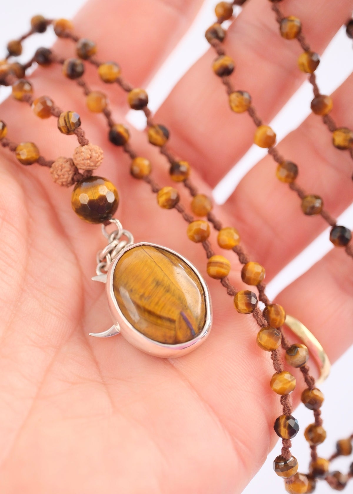 Hand holding Bhaskareya mala with faceted tiger’s eye beads and large sterling silver tiger’s eye pendant