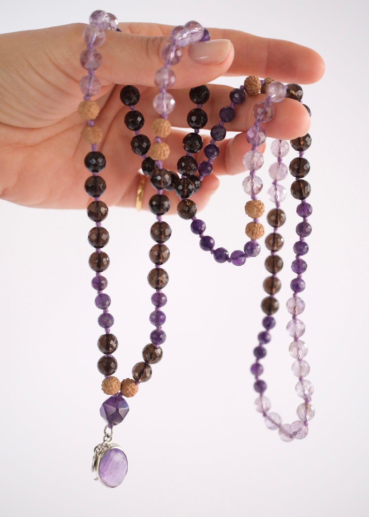 Tejasvi spiritual warrior mala with faceted smoky quartz, amethyst, lavender quartz and amethyst pendant, held by hand.